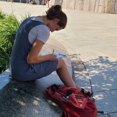 A woman sits by the Martin Luther King Jr Memorial and bends over her notebook.